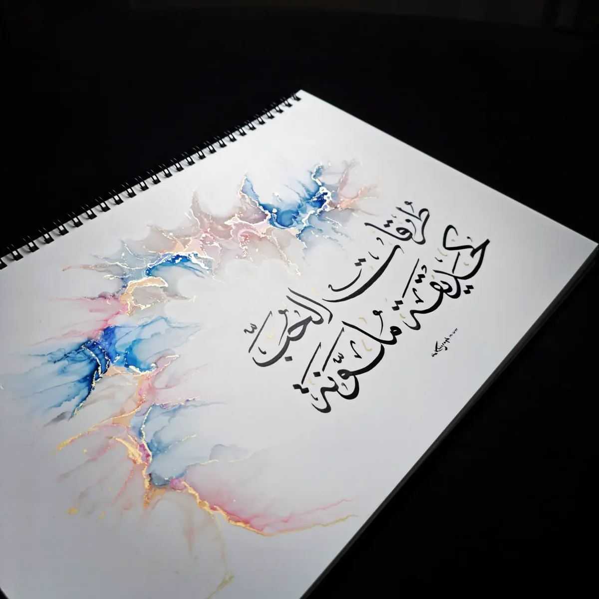 Calligraphie arabe sur un nuage d'encre rose, bleu et or